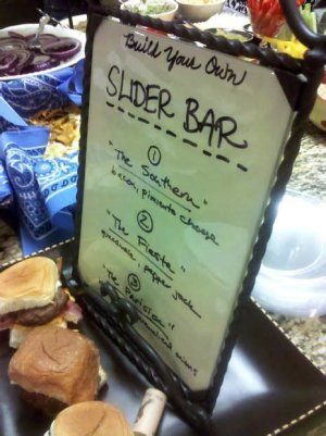 A BBQ slider bar at a wedding reception with small buns and a variety of BBQ meats like pulled pork, brisket, or chicken, along with traditional BBQ sides.