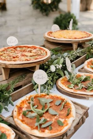 Wedding reception with guests enjoying freshly baked pizzas served on wooden boards around communal tables.