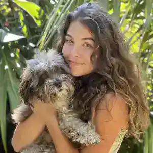 Woman holding a small dog outdoors in a lush, green environment.